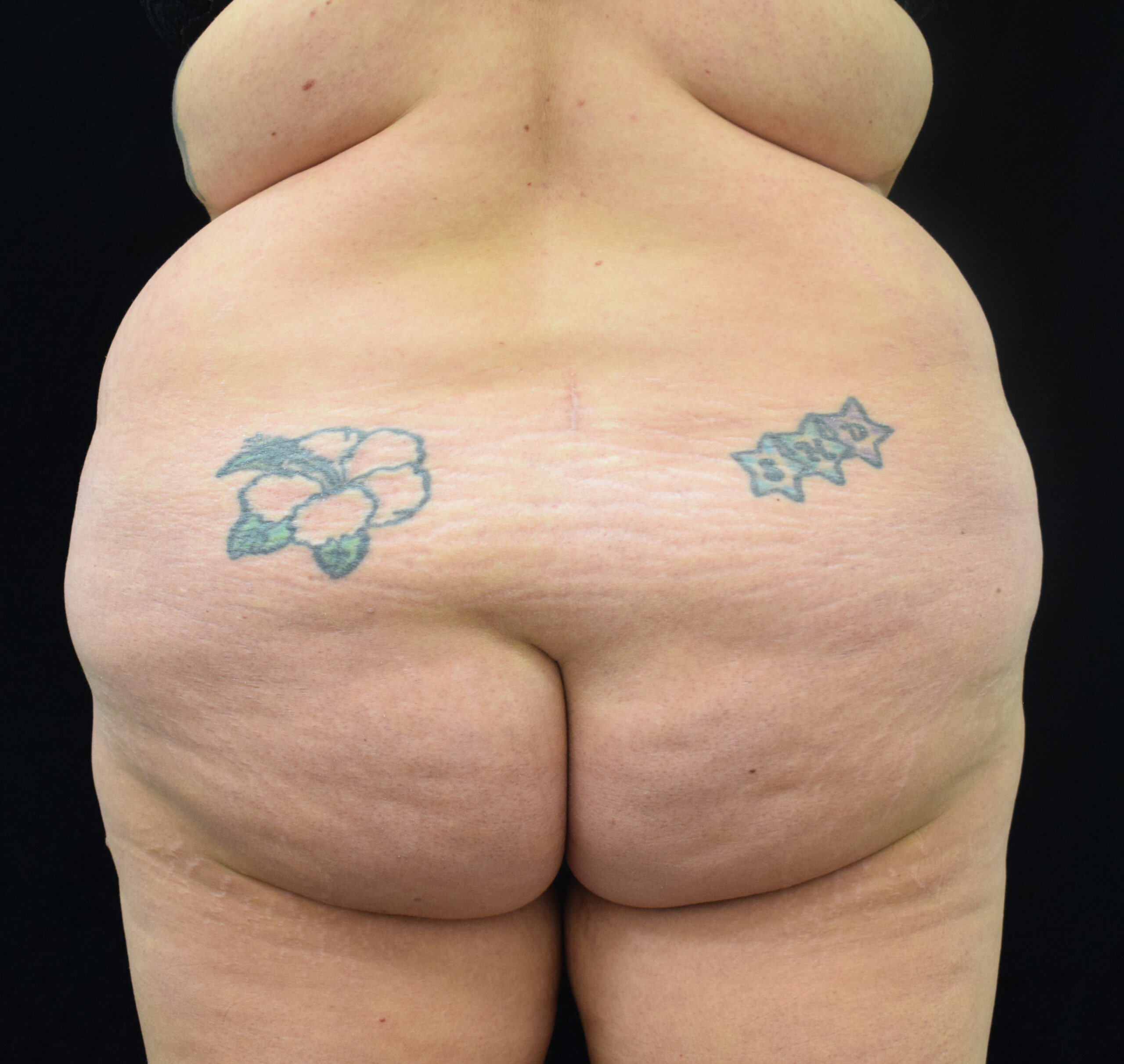 Close-up of a nude adult back and buttocks with multiple tattoos on the lower back, set against a black background.